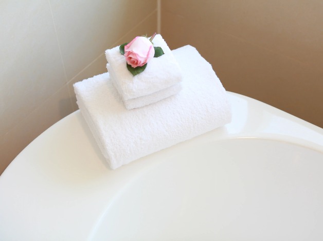 A rose on folded towels on a tub rim.