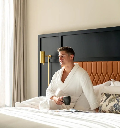 Man with a coffee on Dorsett Melbourne Balcony Suite bed