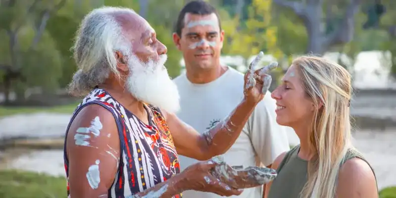 Indigenous elder performing a traditional face painting on tourists.